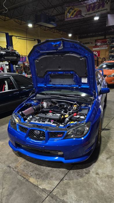 Blue GD Subaru STI with hood up in the shop