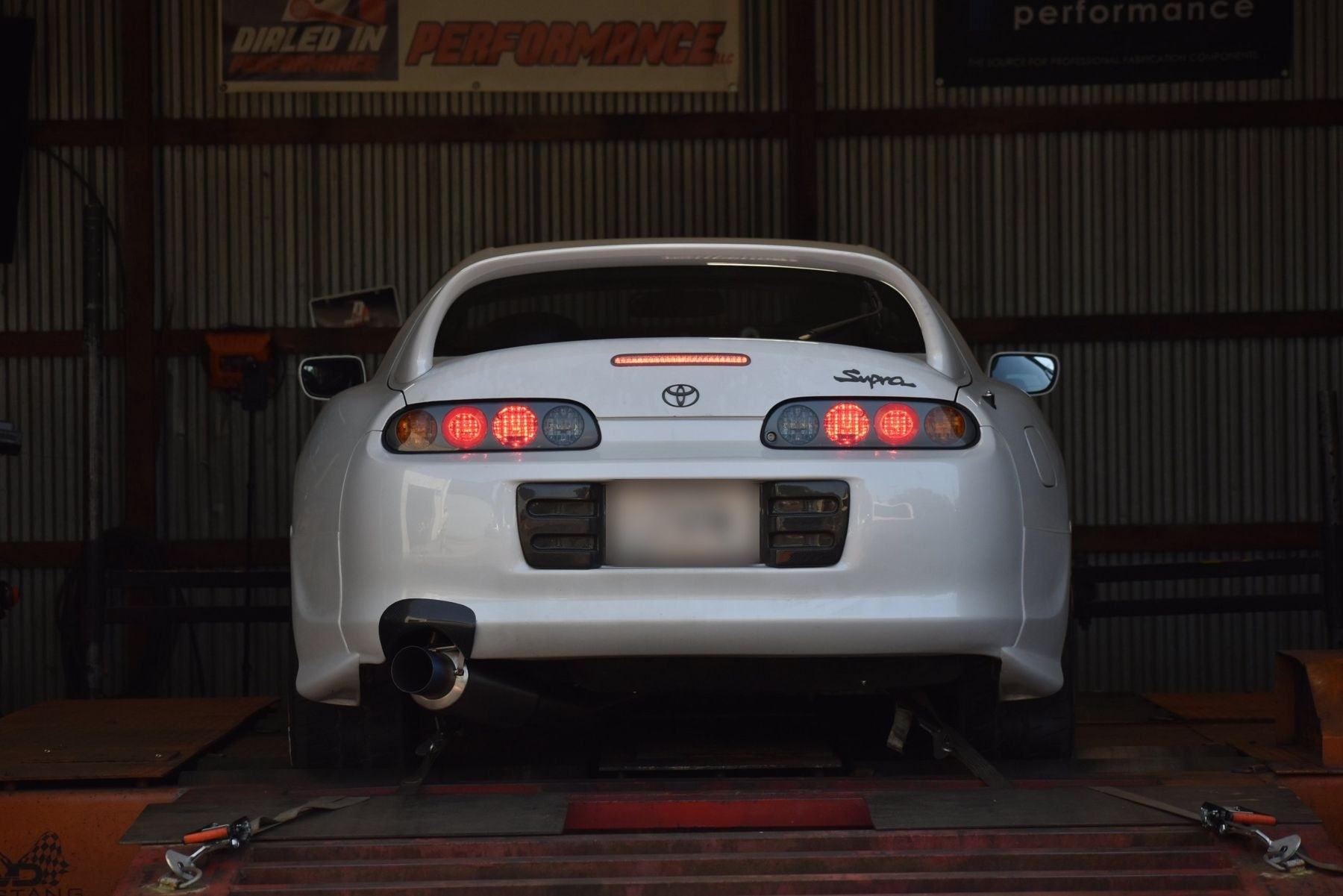 White MKIV Supra strapped to the dyno under the Dialed In Performance banner
